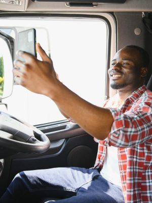 truck driver video call on smartphone in cockpit. Trucker Asian young man beard parked for coffee break after long drive. Worker male driving semi-truck transport logistics express delivery services